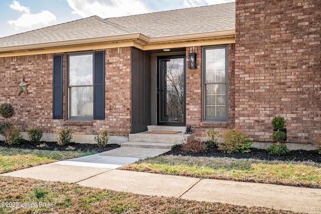 entrance to property with a shingled roof and brick siding