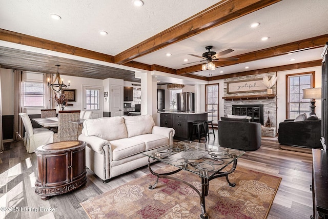 living area featuring beam ceiling, a fireplace, a textured ceiling, and wood finished floors