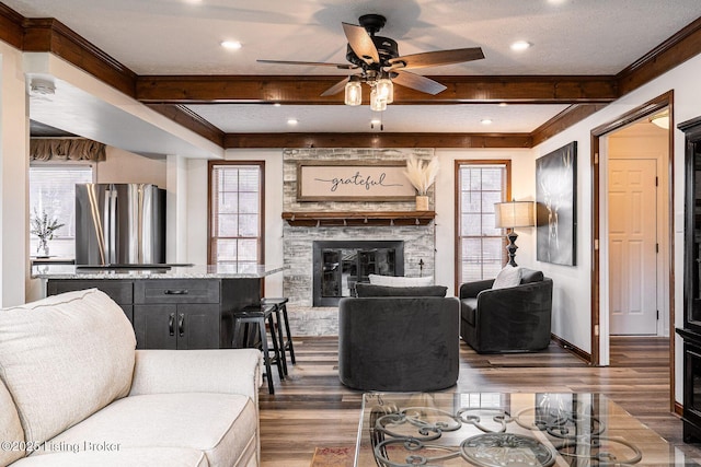 living area with a stone fireplace, beamed ceiling, wood finished floors, and baseboards