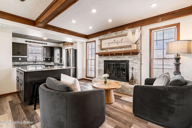 living area with a textured ceiling, a large fireplace, wood finished floors, baseboards, and beamed ceiling