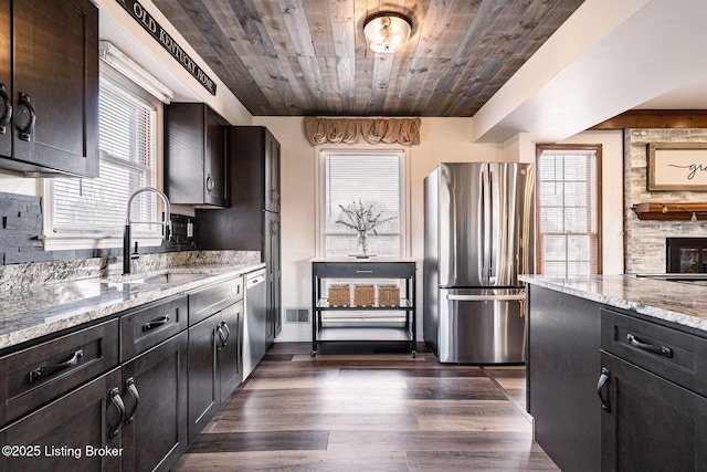 kitchen featuring light stone counters, stainless steel appliances, dark wood-type flooring, wood ceiling, and a sink