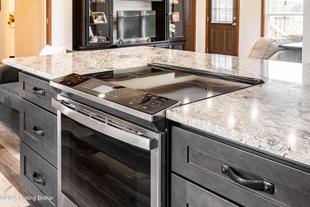 kitchen with glass insert cabinets, wood finished floors, electric range, and light stone countertops