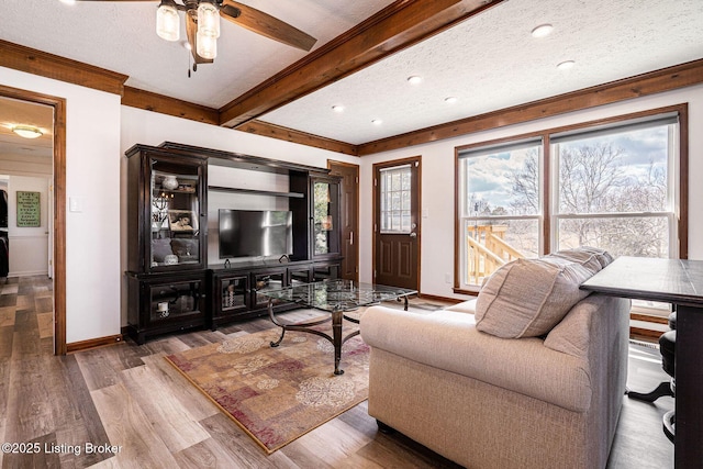 living room featuring baseboards, a ceiling fan, wood finished floors, a textured ceiling, and beam ceiling