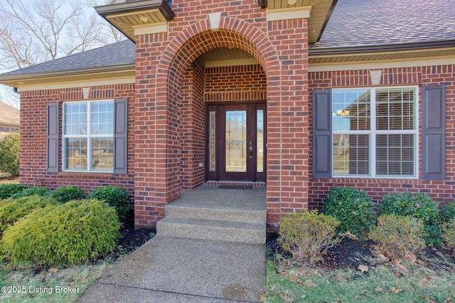 entrance to property featuring a shingled roof and brick siding