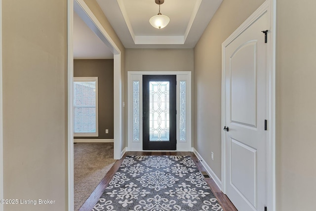 foyer entrance with dark wood-style floors, a tray ceiling, and baseboards