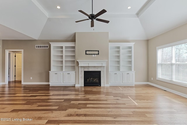 unfurnished living room with lofted ceiling, a tile fireplace, visible vents, baseboards, and light wood finished floors