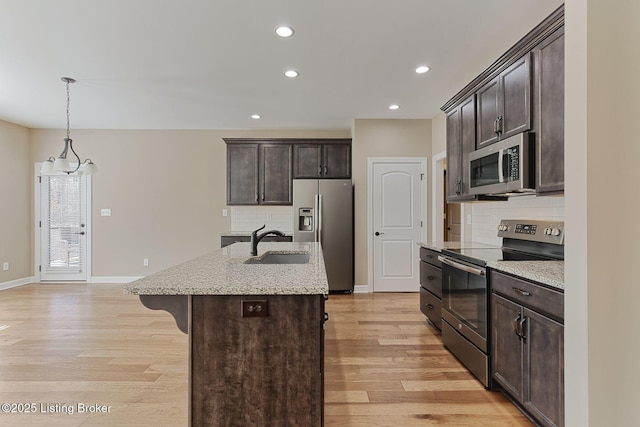 kitchen with a breakfast bar area, a sink, dark brown cabinets, appliances with stainless steel finishes, and light wood finished floors