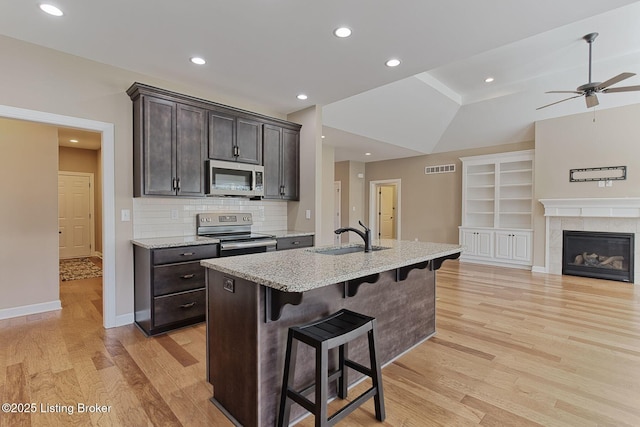 kitchen with appliances with stainless steel finishes, a sink, light wood-style flooring, and a breakfast bar area