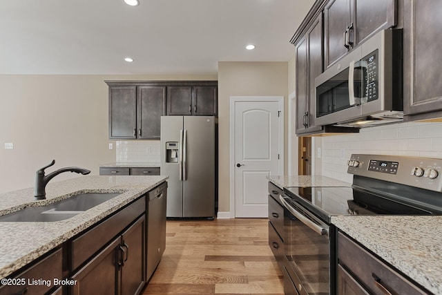 kitchen with light wood finished floors, appliances with stainless steel finishes, dark brown cabinets, and a sink