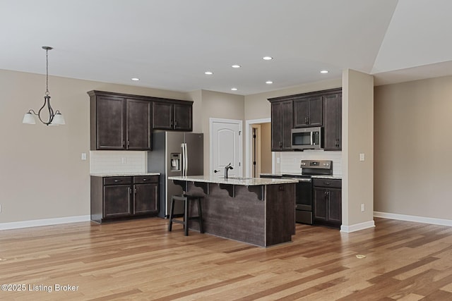 kitchen featuring light wood finished floors, appliances with stainless steel finishes, a sink, dark brown cabinets, and a kitchen bar