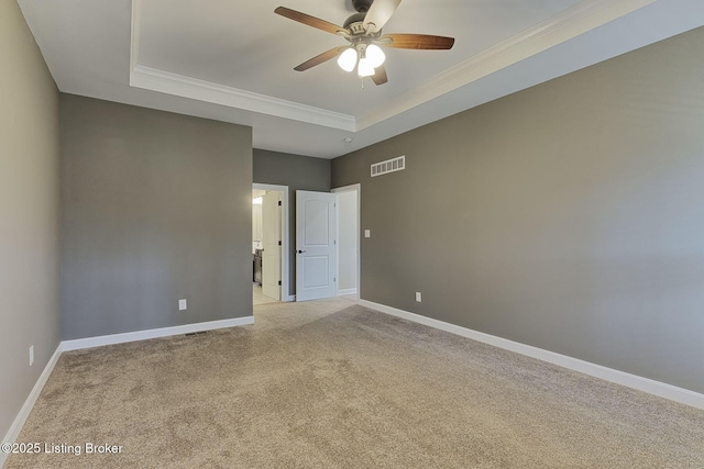 empty room featuring a tray ceiling, light colored carpet, visible vents, ornamental molding, and baseboards