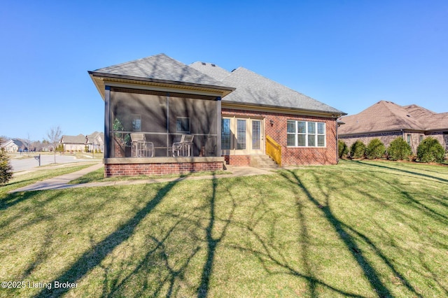 rear view of house featuring entry steps, a sunroom, roof with shingles, a yard, and brick siding