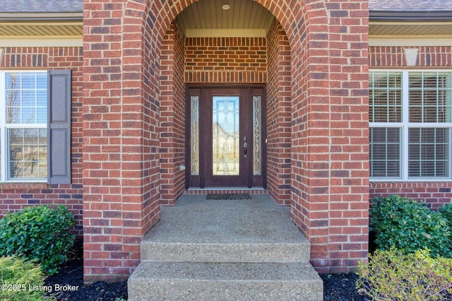 entrance to property featuring a shingled roof and brick siding