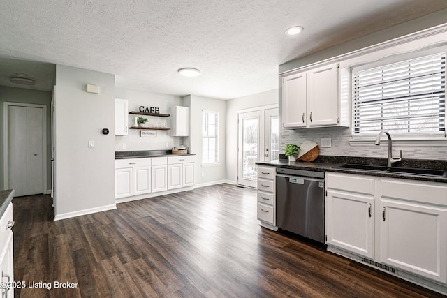 kitchen featuring dark countertops, dark wood-style floors, stainless steel dishwasher, white cabinetry, and a sink