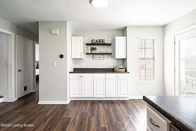 bar featuring visible vents, dark wood-type flooring, a textured ceiling, bar area, and baseboards