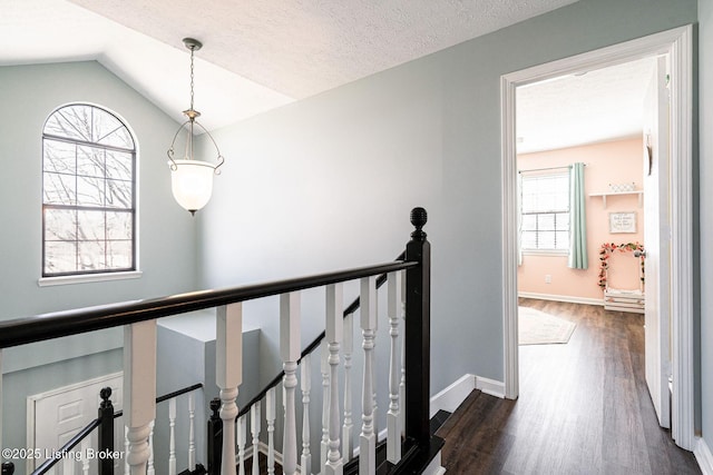 hall featuring a textured ceiling, lofted ceiling, an upstairs landing, baseboards, and dark wood-style floors