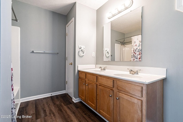 full bath featuring double vanity, a sink, baseboards, and wood finished floors