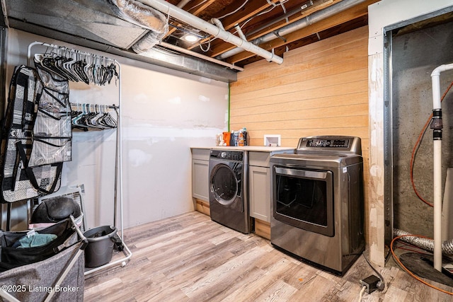 clothes washing area featuring light wood finished floors, wood walls, cabinet space, and washer and dryer