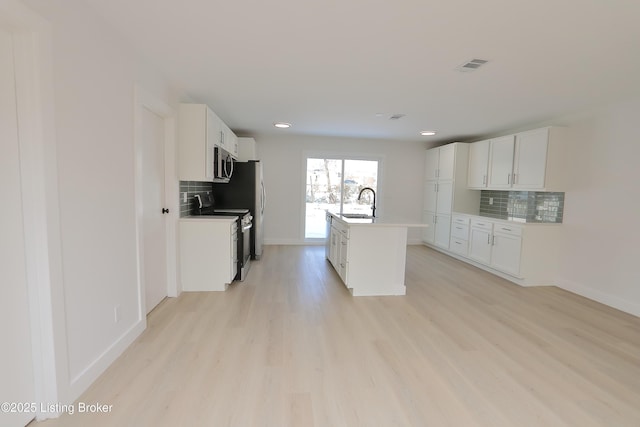 kitchen featuring a center island with sink, appliances with stainless steel finishes, light countertops, light wood-style floors, and white cabinetry