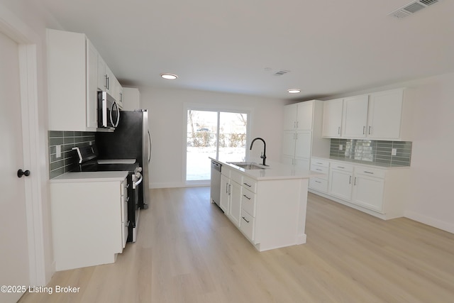 kitchen with stainless steel appliances, light countertops, visible vents, a kitchen island with sink, and a sink