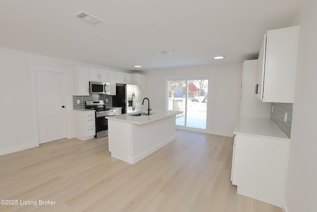 kitchen featuring visible vents, white cabinets, a kitchen island with sink, stainless steel appliances, and light countertops