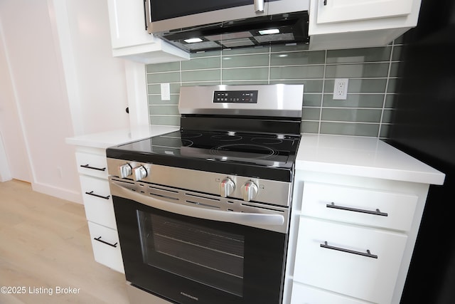 kitchen featuring decorative backsplash, appliances with stainless steel finishes, light countertops, light wood-type flooring, and white cabinetry