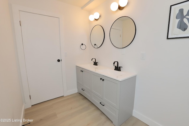 full bathroom with double vanity, baseboards, a sink, and wood finished floors