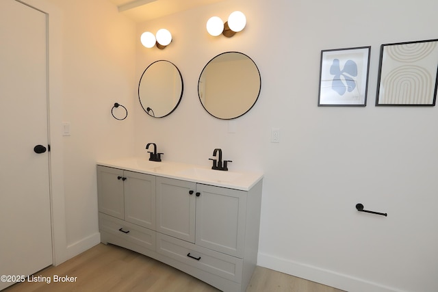 bathroom with a sink, double vanity, baseboards, and wood finished floors