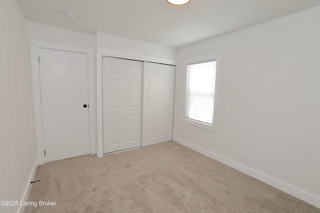 unfurnished bedroom featuring baseboards, a closet, and light colored carpet