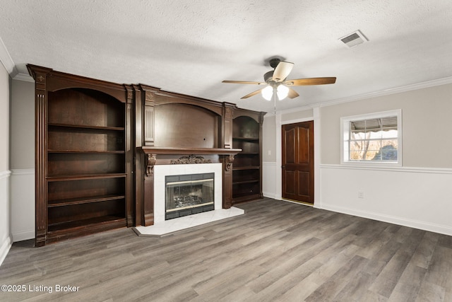 unfurnished living room with a textured ceiling, a tile fireplace, wood finished floors, visible vents, and crown molding