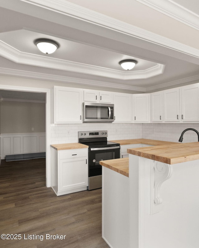 kitchen featuring butcher block countertops, dark wood-type flooring, a tray ceiling, stainless steel appliances, and white cabinetry