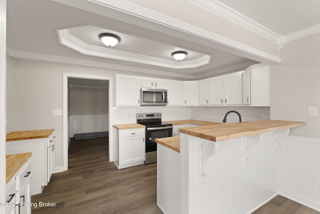 kitchen featuring white cabinets, stainless steel appliances, a kitchen bar, and wooden counters