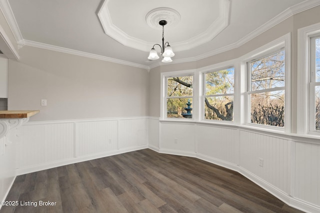 unfurnished dining area with a wainscoted wall, a tray ceiling, a chandelier, and dark wood-type flooring