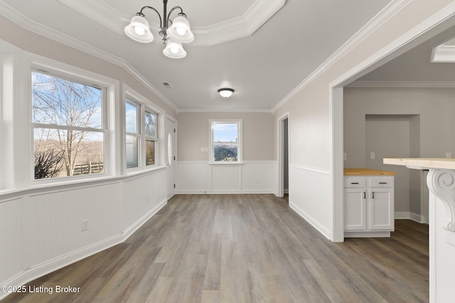 unfurnished dining area featuring a chandelier, wainscoting, light wood-type flooring, and crown molding