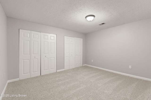 unfurnished bedroom featuring carpet, two closets, visible vents, and baseboards