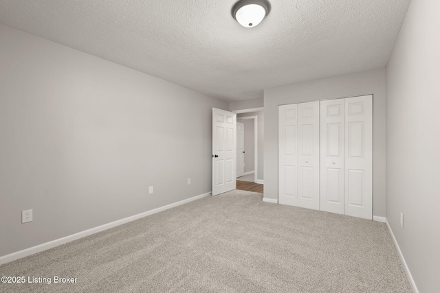 unfurnished bedroom with carpet, a closet, a textured ceiling, and baseboards