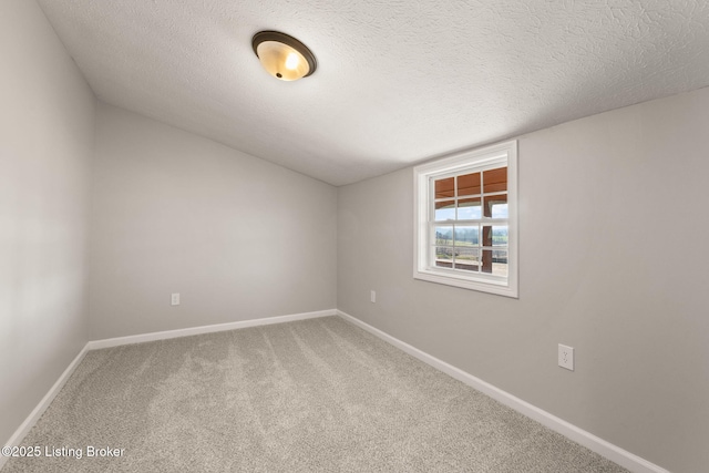 carpeted empty room with a textured ceiling, vaulted ceiling, and baseboards