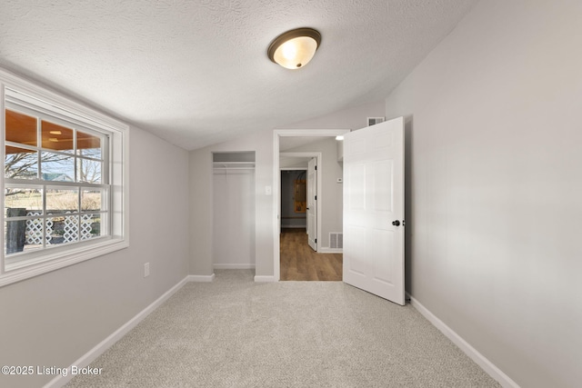 unfurnished bedroom with a textured ceiling, light carpet, baseboards, vaulted ceiling, and a closet