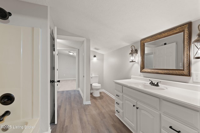 full bathroom featuring vaulted ceiling, a textured ceiling, vanity, wood finished floors, and baseboards