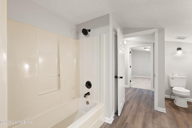 bathroom featuring bathing tub / shower combination, visible vents, toilet, a textured ceiling, and wood finished floors