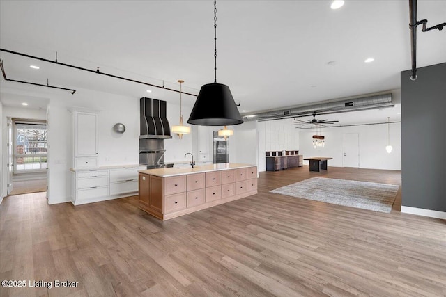 kitchen featuring a spacious island, white cabinetry, light countertops, hanging light fixtures, and wall chimney exhaust hood