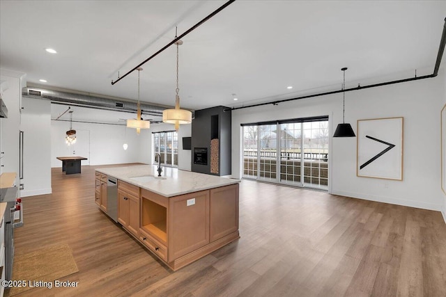 kitchen with light stone counters, a kitchen island with sink, a sink, open floor plan, and hanging light fixtures