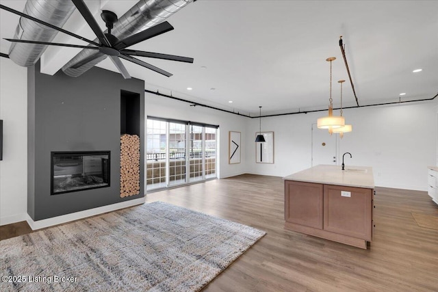 kitchen with light wood-style flooring, a sink, open floor plan, a glass covered fireplace, and decorative light fixtures