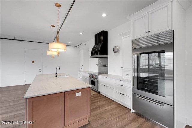 kitchen with wall chimney exhaust hood, high end appliances, white cabinetry, and pendant lighting