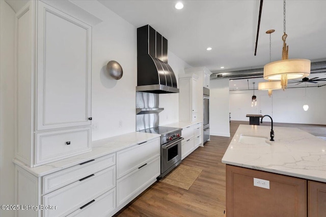 kitchen featuring pendant lighting, stainless steel stove, white cabinets, and wall chimney range hood