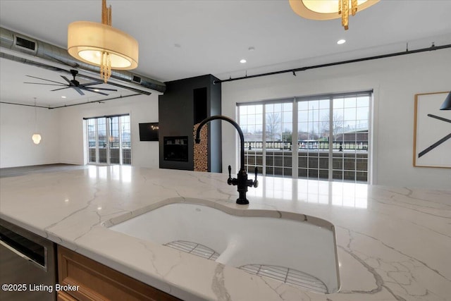 kitchen featuring open floor plan, decorative light fixtures, light stone countertops, a fireplace, and a sink