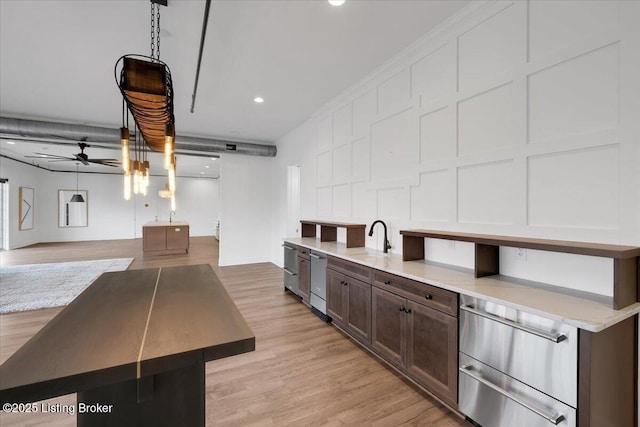 kitchen with ceiling fan, dark brown cabinetry, light wood-style floors, hanging light fixtures, and an island with sink