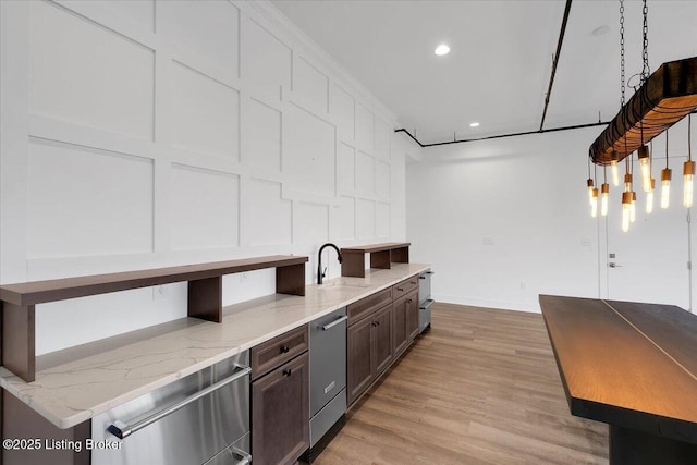 kitchen featuring pendant lighting, light wood finished floors, dark brown cabinetry, a sink, and dishwasher