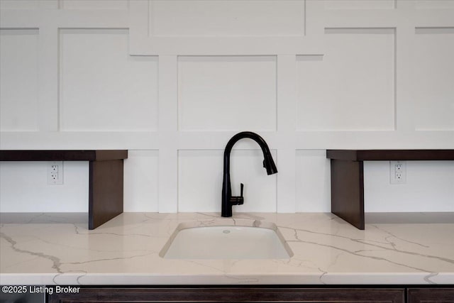 interior details with light stone counters, a sink, and white cabinets