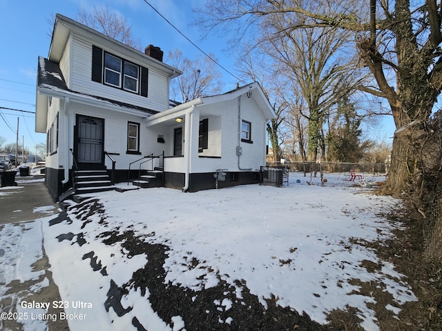 view of front of home featuring brick siding, a chimney, and fence